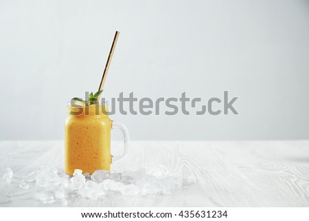 Man hand takes transparent rustic jar with tasty healthly freshly made yellow smoothie from mango, pineapple, banana and passion fruit. Melted ice around isolated on white table Easy to repaint Royalty-Free Stock Photo #435631234