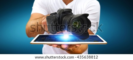 Young man holding modern digital camera over his digital tablet