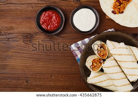 Burritos wraps with meat, beans and vegetables on wooden board