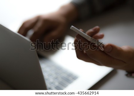 Man holding Telephone in front of Laptop in dark warm tones with focus on edge of phone Royalty-Free Stock Photo #435662914