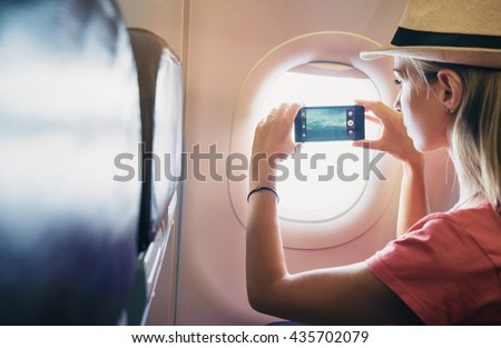 Travel and technology. Young woman in plane taking photo on her smartphone while sitting in airplane seat. Focus on phone.