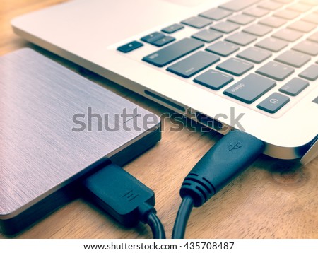 External or portable hard drive (HDD) connected to laptop computer for transfer or backup data on wooden texture office desktop Royalty-Free Stock Photo #435708487