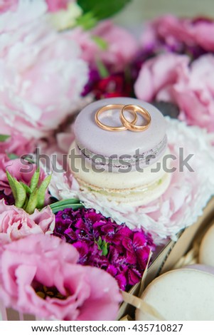 Set of colorful macaroon with wedding or engagement rings on top  in the box with flowers. Decorated gift box with dessert cookies. Close up, selective focus.