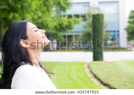Closeup portrait, young woman in white shirt breathing in fresh crisp air after long day of work, isolated outdoors outside background. Stop and smell the roses, connect with nature Royalty-Free Stock Photo #435747925