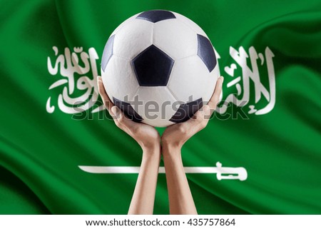 Image of two hands lifting a soccer ball with flag background of Saudi Arabia