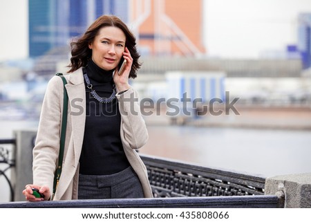 european beautiful middle-aged woman talking on the phone and smiling outdoors. business. fashion
