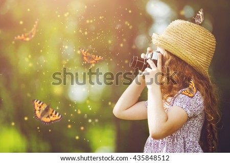 Little girl in straw hat, rustic style dress, photographing butterfly with retro photo camera in fairytale forest.