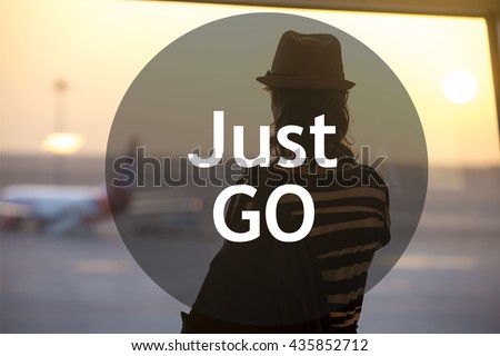 Young woman in straw hat waiting for flight in modern airport terminal building. Watching airplanes in window on sunrise or sunset. Rear view with motivational text "Just go"