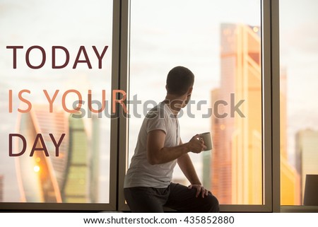 Rear view of young man sitting on window with coffee cup looking at dawn city scenery. Handsome casual guy relaxing with hot drink. Motivational text "Today is your day"