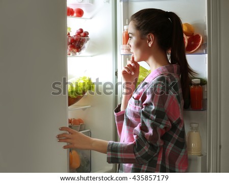 Young beautiful woman looking into fridge at night Royalty-Free Stock Photo #435857179