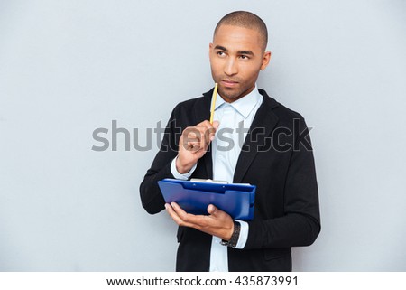 Thoughtful african american young man writing on clipboard