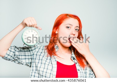 close-up of a bright red-haired girl yawns with a retro alarm clock