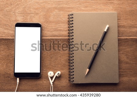Smartphone with white screen and Note book On Wooden Table With Copyspace