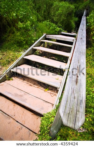 An old wooden staircase and walkway leading into a lush green forest. Shallow Depth of field with focus on the banister
