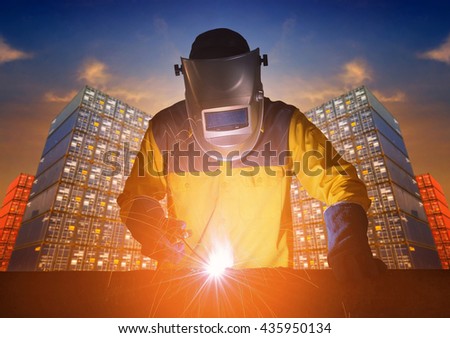 Industrial welding worker welding steel structure with cargo container stack in background.