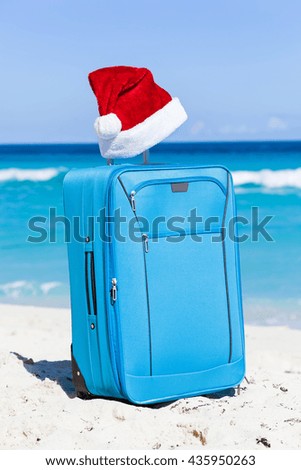 Christmas red hat on handle travel luggage with tropical beach and turquoise sea background. New Year holidays concept