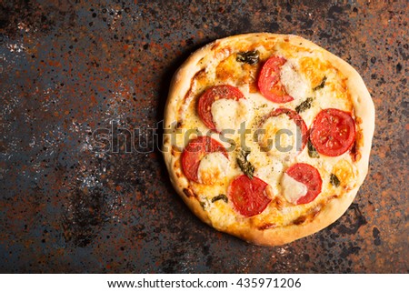 Pizza Margherita with tomatoes and mozzarella cheese on a rust effect surface