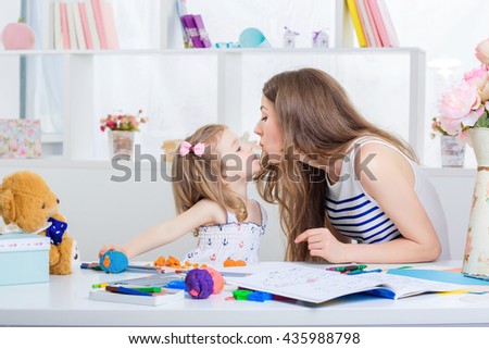 beautiful young mother and her little daughter playing with colored plasticine and drawing with crayons on the album.  mother kissing baby
