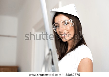 A beautiful young adult woman painting a wall in her home in white.
