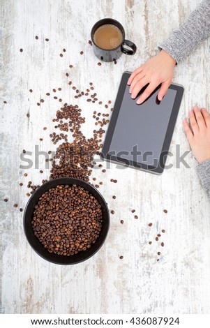 A womanÃ¢??s hand using a tablet next to coffeebeans on the table