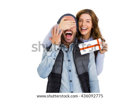 Close up of woman covering mans eyes while giving him a surprise gift on white background