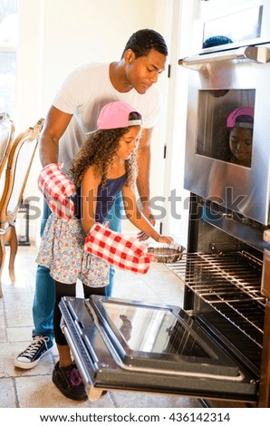 Father helping daughter insert cake tin into oven