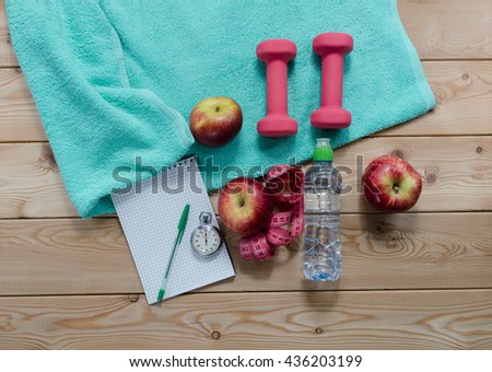 Healthy lifestyle concept. colored Apples notepad stopwatch dumbbells measure tape sport water bottle and turquoise towel on wooden table