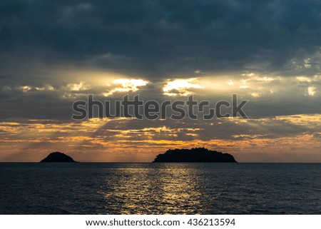 silhouette of the islands to the shining sea under dramatic dark clouds that make their way through the rays of sunlight at sunset