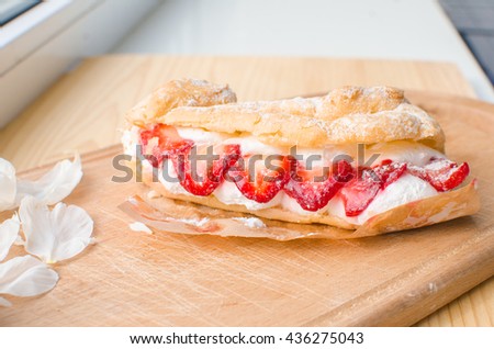 
eclairs with strawberry and sweet cream protein . peonies and eclair on a wooden board. refined desserts.