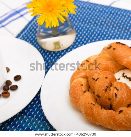 sweet bun on a white plate. cup of coffee on a white plate. coffee beans, cinnamon stick. dandelion flowers in a small vase