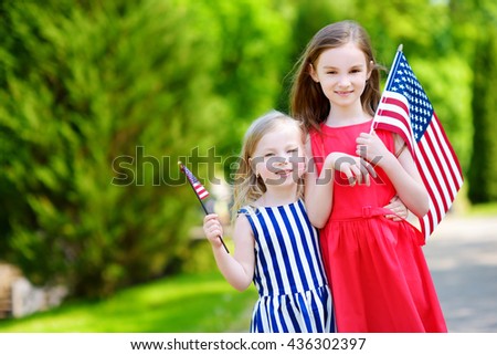 Two adorable little sisters holding american flags outdoors on beautiful summer day. Independence Day concept.