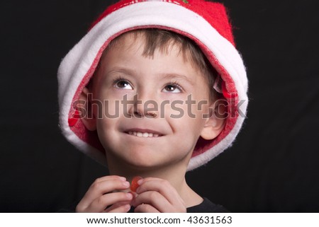 Young boy wearing Santa Claus hat, holding piece of candy, posed against black background