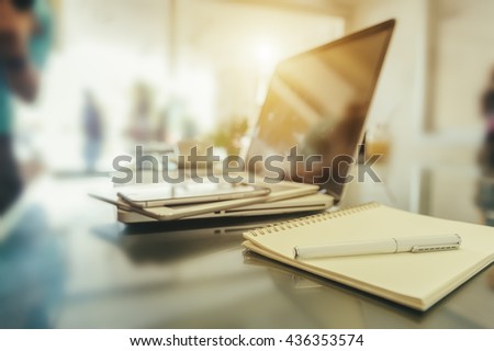 A pen on notebook in office workplace with laptop and mobile phone with shallow depth of field. (soft focus)