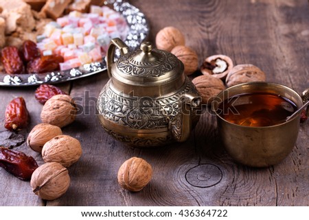 Traditional arabic tea set, walnut and dried dates. Oriental sweet on silver plate. Turkish delight, halva, dates and others on old wooden background