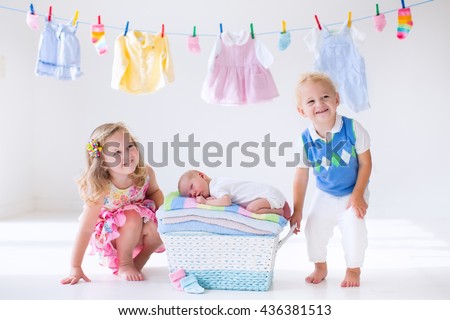 Newborn child on a pile of clean dry towels. Brother and sister kissing little sibling. Siblings bonding. Twin toddler kids kiss baby boy. New born kid after bath in a towel. Family washing clothes. 