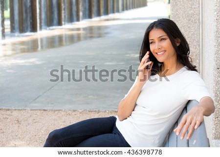 Closeup portrait, young, happy beautiful woman in white shirt sitting, speaking on cell phone, sitting on park bench, isolated outside outdoors background. Good news