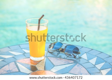 Orange juice with sunglasses on color stone table near pool