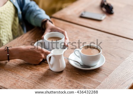 Two cups of coffee with woman hands on the wooden table in cafe background