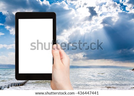 travel concept - tourist photographs sumbeams over Dead Sea on tablet pc with cut out screen with blank place for advertising