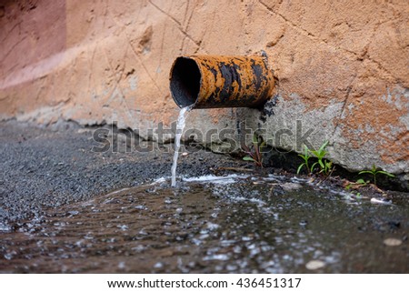 Rusty pipe with flowing rain water. Close up of water gushing out of the pipe. Water flowing from pipe against blurred brick background