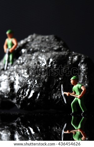 Coal miniature miners / miniature model miners on a piece of coal on a carbon fiber background