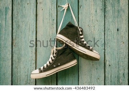 Dark blue sneakers hang on a nail on a blue wooden wall, canvas shoe,toning