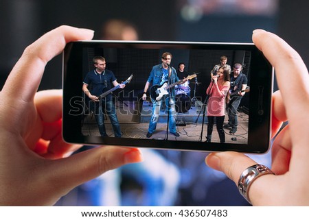 Music band performance photographing on smartphone. Closeup of smartphone screen with picture of young student rock band performance in sound recording studio