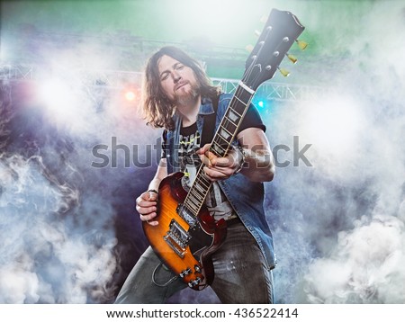 Rock band performs on stage. Guitarist, bass guitar and drums. The guitarist plays solo. Royalty-Free Stock Photo #436522414
