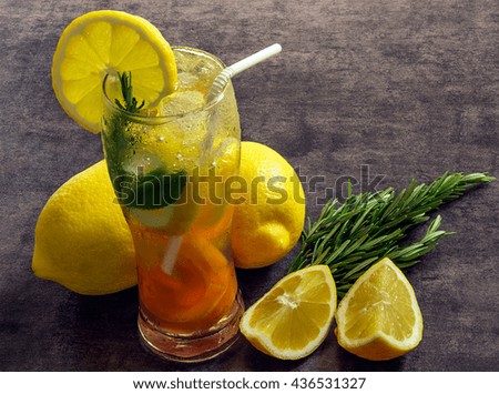 Fresh iced lemonade in a glass with slices of lemon, apricot, mint and rosemary. On a dark background.