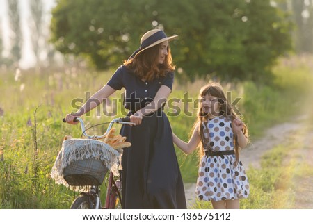 Beautiful mother and daughter on a walk with the bike, carry bread in a basket