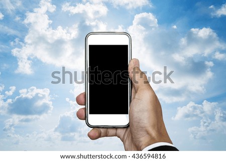 Hand holding mobile phone with blank space on screen, on blue sky with white clouds and bright light behind