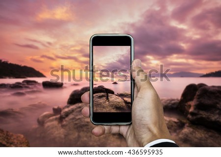 Hand holding smart phone taking photo of sunset landscape in vertical composition, in summer vacation time