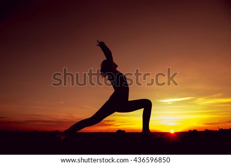 Young girl yoga on the roof. Silhouette at the sunset