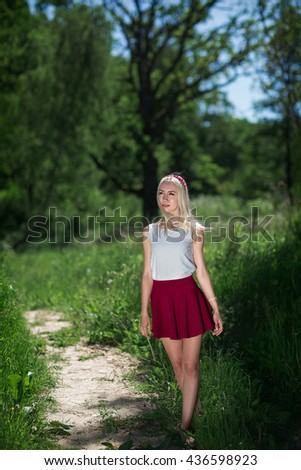 The young girl walks on a grass. The girl is dressed in a white blouse and a red skirt. The girl walks on footpaths.